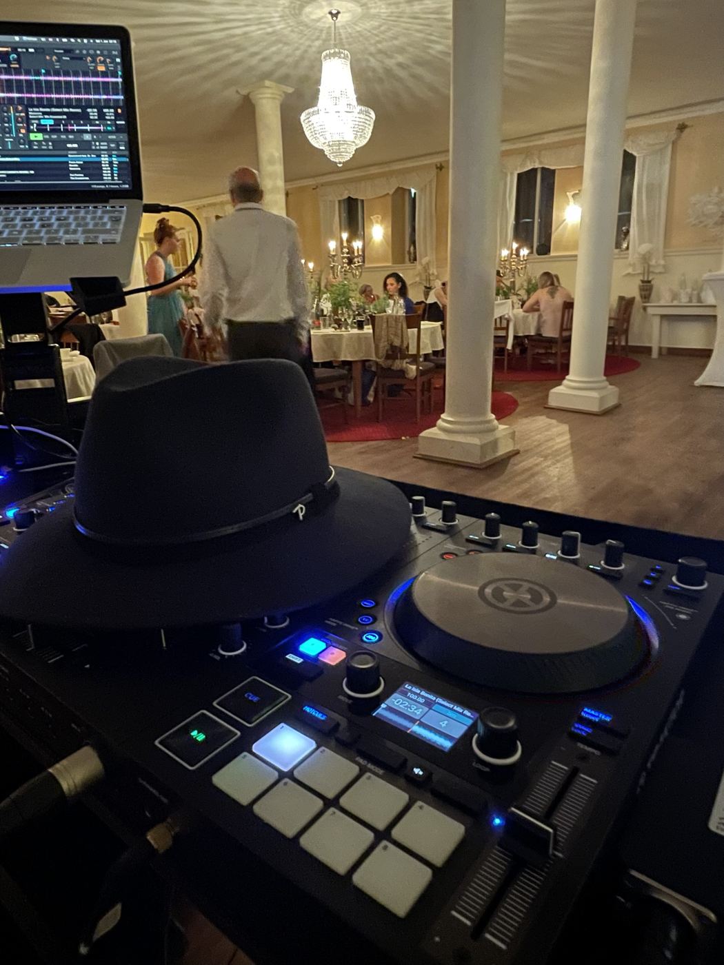DJ-Pult mit schwarzem Hut in festlichem Saal mit Kronleuchter