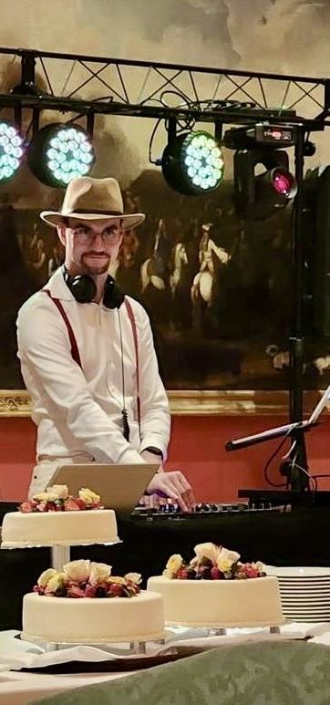 Paul am DJ-Pult vor Gemälde, im Vordergrund Hochzeitstorten